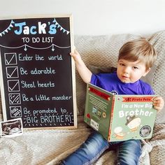 a little boy sitting on a couch reading a book next to a chalkboard sign that says jack's to do list