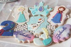 some decorated cookies are on a plate with snowflakes and princesses in the background