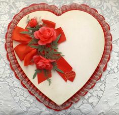 a heart shaped card with red flowers and ribbon on the front, sitting on a lace doily