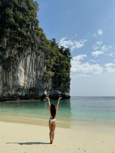 a woman standing on top of a sandy beach next to the ocean with her arms in the air