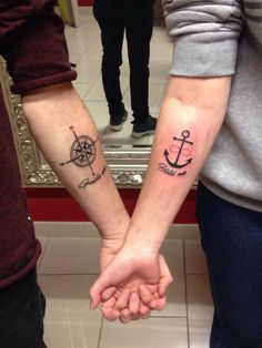 two people holding hands with tattoos on their arms and one has an anchor, the other is a compass