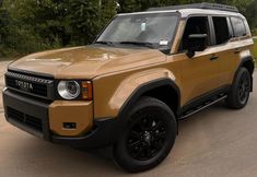 a tan and black suv parked on the side of a road in front of trees