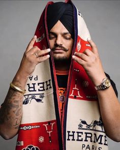 a man wearing a scarf with his hands on his head and holding something in front of his face