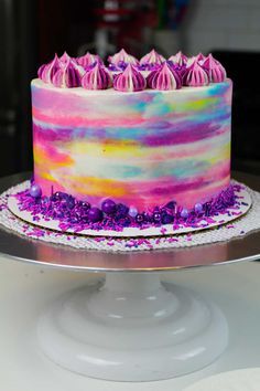 a multi - colored cake with purple frosting and sprinkles on top