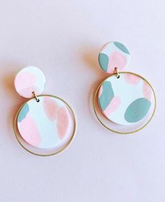 two circular earrings with pink, blue and green designs on them are hanging from gold hoops