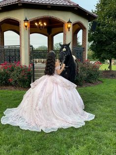 a woman in a wedding dress sitting on the grass next to a black horse and gazebo