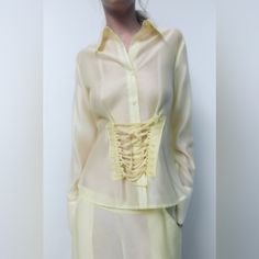 Lapel Collar Shirt With Long Cuffed Sleeves. Corset Detail With Self Lacing. Front Button Closure. 74% Lyocell 26% Polyamide Elegant Yellow Summer Shirt, Elegant Yellow Summer Blouse, Chic Yellow Blouse With Button Closure, Elegant Yellow Tops For Summer, Elegant Yellow Summer Tops, Fitted Yellow Shirt With Buttons, Fitted Long Sleeve Yellow Blouse, Yellow Casual Party Blouse, Casual Yellow Party Blouse