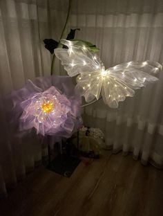 two lighted flowers sitting on top of a wooden floor next to a curtained window