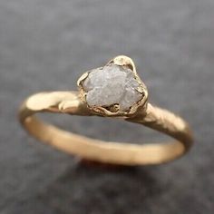 a gold ring with a white diamond in the center on a black surface and grey background