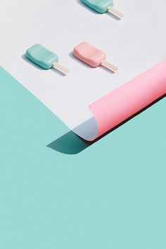 three popsicles sitting on top of a piece of paper with pink and blue sticks sticking out of it