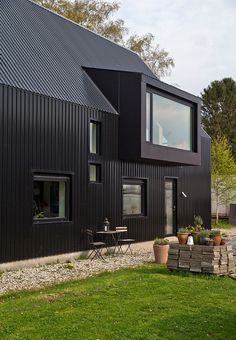 a black house with lots of potted plants and chairs in front of the windows