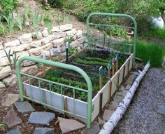 an old metal bed filled with lots of plants next to a stone wall and grass