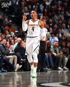 a basketball player holding his hand up in the air while walking on a court with people watching