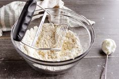 a glass bowl filled with flour next to a whisk and spoon on top of a wooden table