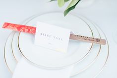 a place setting with red and white napkins, gold rimmed plates and an orange flower