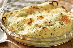 a casserole dish with cheese and herbs in it on a wooden table next to two spoons