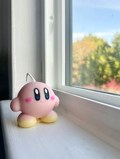 a small pink toy sitting on top of a window sill next to a window