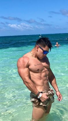 a shirtless man standing in the ocean with his hands on his hips and sunglasses on