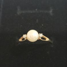 a pearl and diamond ring sitting on top of a black surface