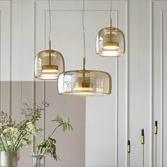 three lights hanging from the ceiling above a table with flowers and vases on it