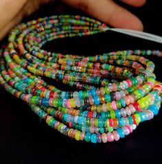 multicolored glass beads are being held by a person's hand on a black surface