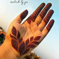 a person's hand with a tattoo that has leaves painted on it and the sky in the background