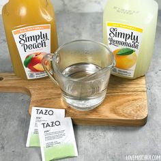 two bottles of simply peach tea on a cutting board next to a glass cup with liquid in it