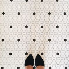 a woman's feet in black shoes standing on a tiled floor with hexagonal tiles