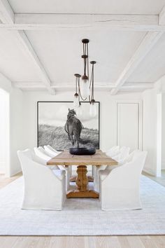 a dining room table with white chairs and a painting on the wall in the background