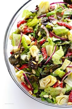 a salad with red onions, lettuce and pine nuts in a glass bowl