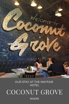 two people sitting at a table in front of a sign that reads coconut grove, our stay at the may fair hotel