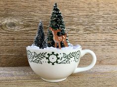 a white cup filled with small trees and reindeer figurines on top of it