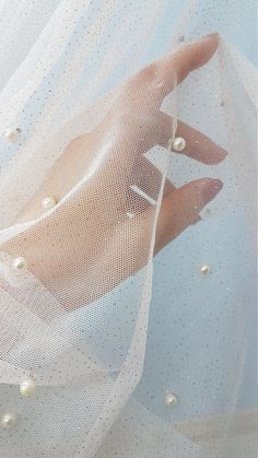 a woman's hand is seen through the veil of a white dress with pearls on it