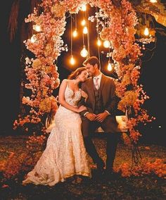 a man and woman are sitting on a bench in front of a tree with lights