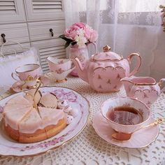 a table topped with pink tea cups and saucers filled with cake next to a vase full of flowers