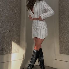 a woman is posing in a white suit and black boots