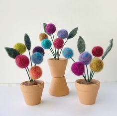 three potted plants with different colored yarn balls in them on a white table top