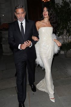 a man and woman dressed in formal wear walking down the street at an event together