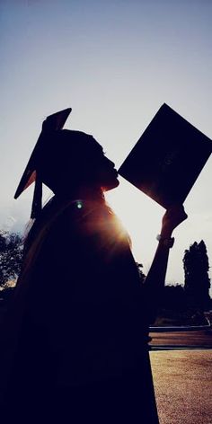 the silhouette of a person wearing a graduation cap and gown holding a book in their hands