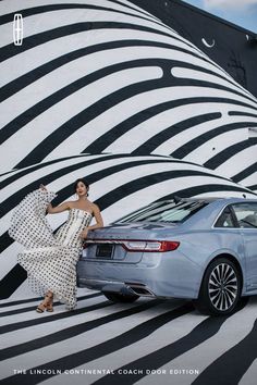 a woman standing next to a car in front of a zebra print wall