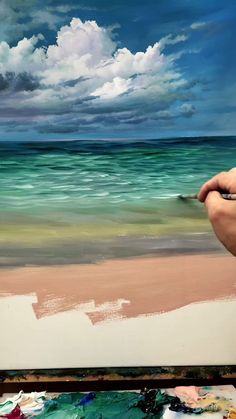 someone is painting on the beach with blue skies and white clouds in the background,