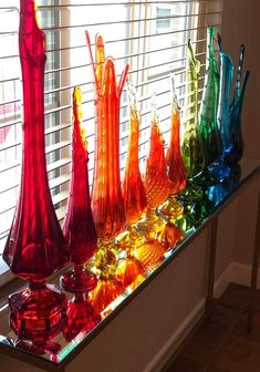 colorful glass vases are lined up on a window sill in front of the blinds