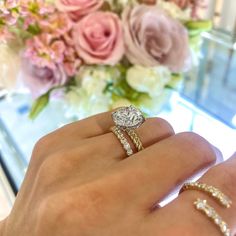 a woman's hand with two rings on it and a bouquet of flowers in the background