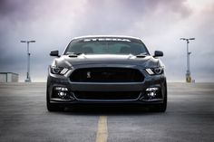 the front end of a black mustang parked in an empty parking lot with lights on