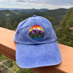 a blue hat sitting on top of a wooden rail next to a tree filled mountain