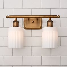 two light fixtures mounted on a white brick wall in a bathroom with brass fixtures and glass shades