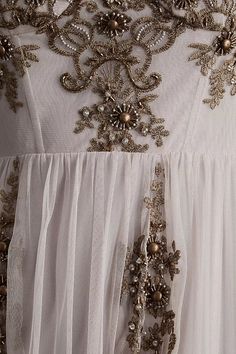 the back of a white dress with gold beading and sequins on it