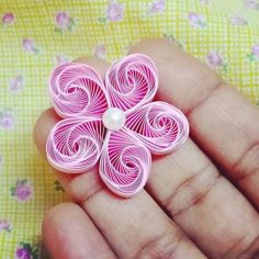 a hand holding a pink flower brooch with a pearl in the center on a yellow background