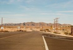 an empty road in the middle of nowhere with mountains in the backgrouds