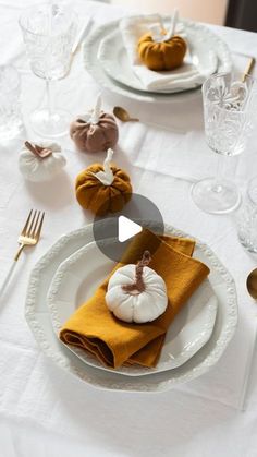 the table is set with white plates and gold napkins, silverware, and pumpkins